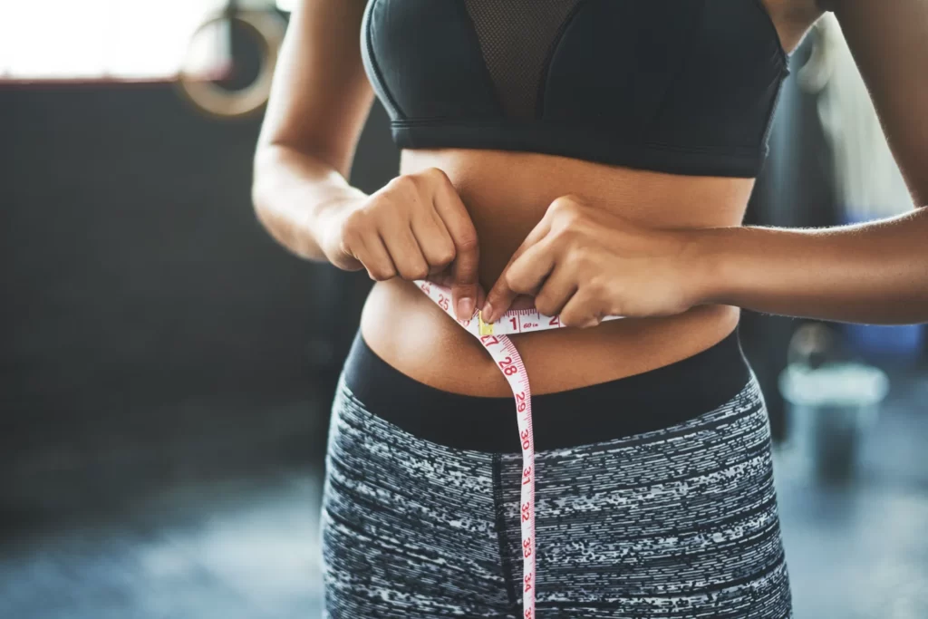 fit woman measures waist in fitness studio utc
